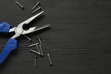 Needle nose pliers and nails on black wooden table, flat lay. Space for text