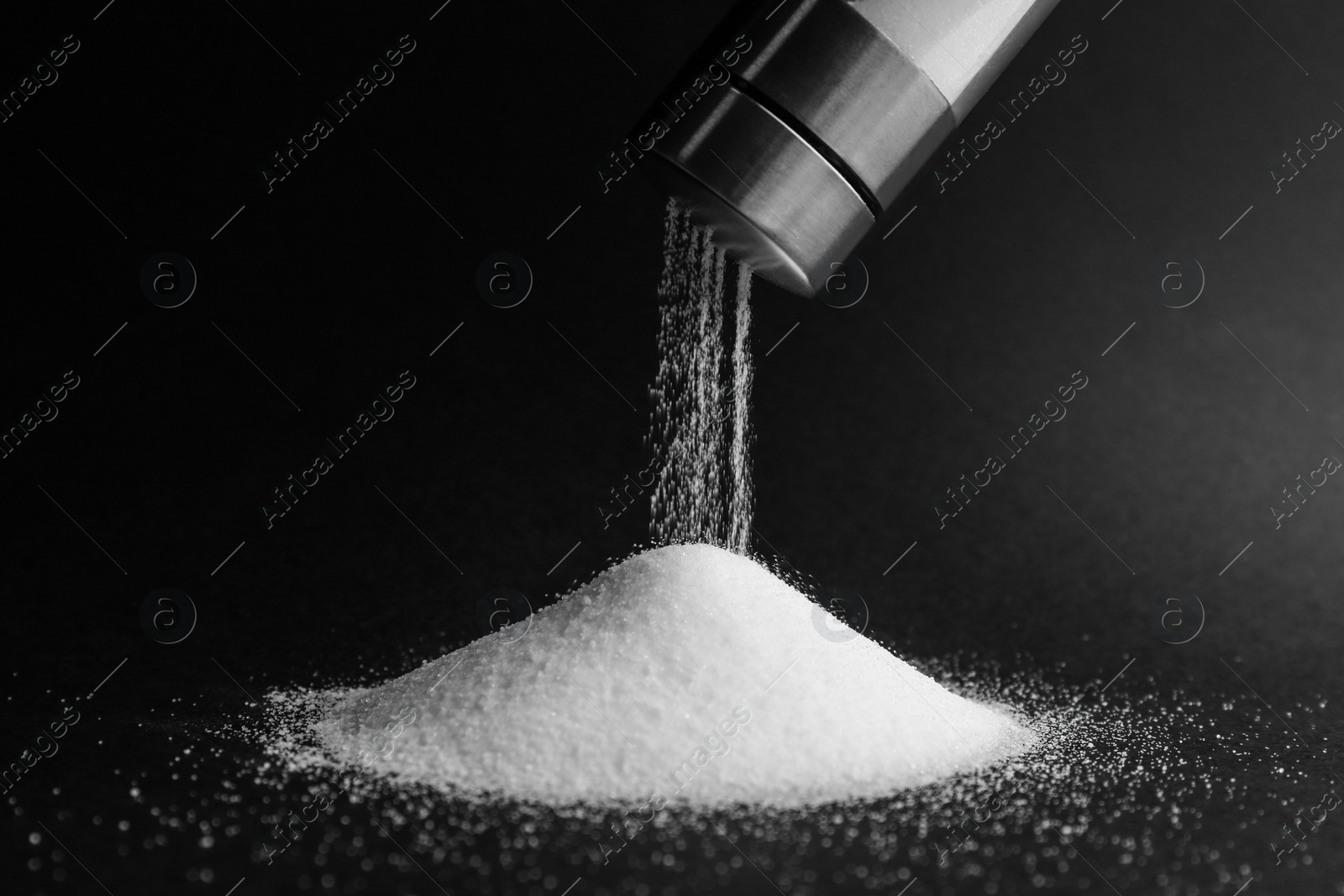 Photo of Pouring salt from shaker on black background, closeup