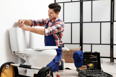 Photo of Professional plumber working with toilet bowl in bathroom