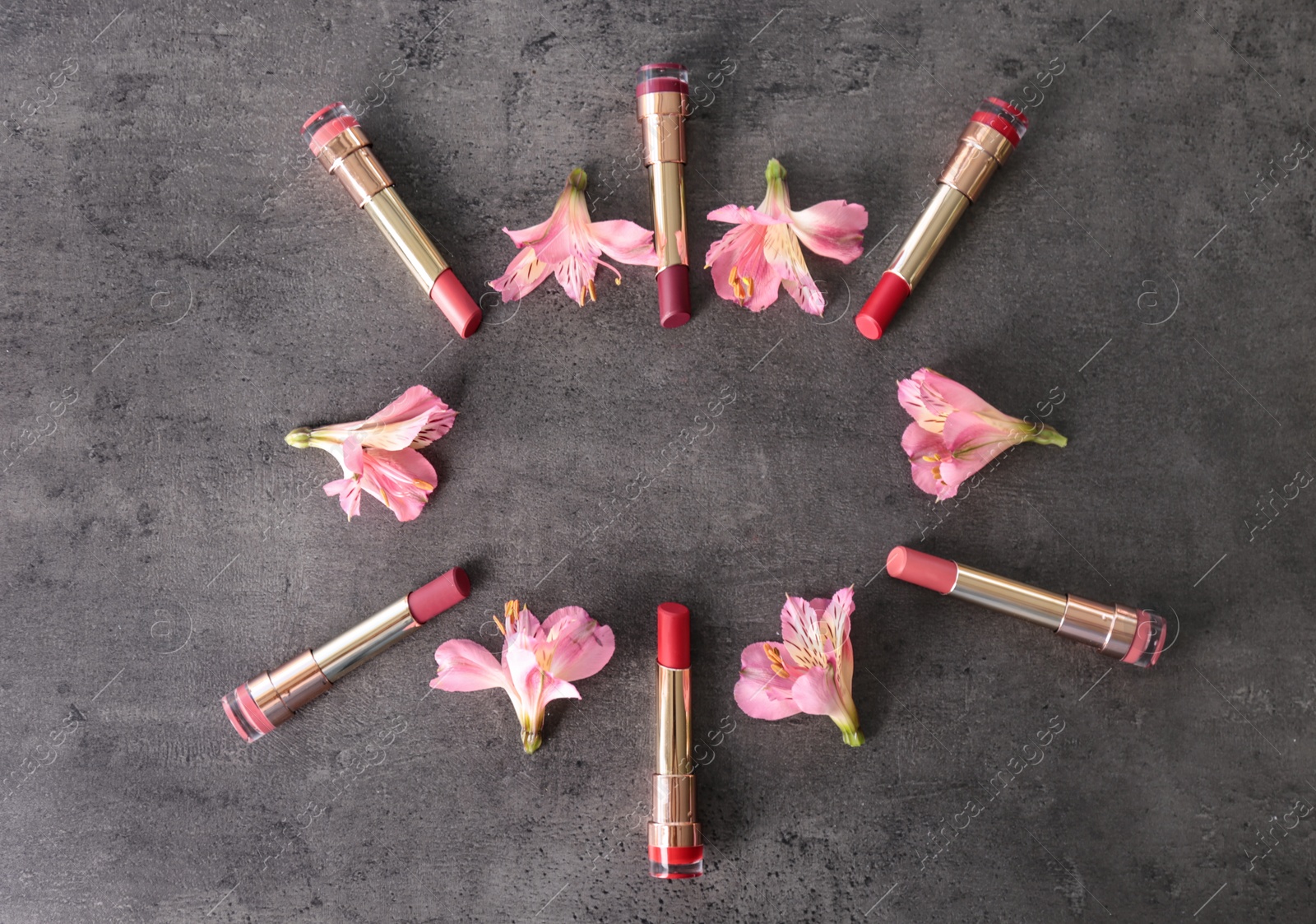 Photo of Frame made with bright lipsticks and spring flowers on grey table, flat lay. Space for text