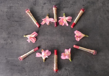 Frame made with bright lipsticks and spring flowers on grey table, flat lay. Space for text