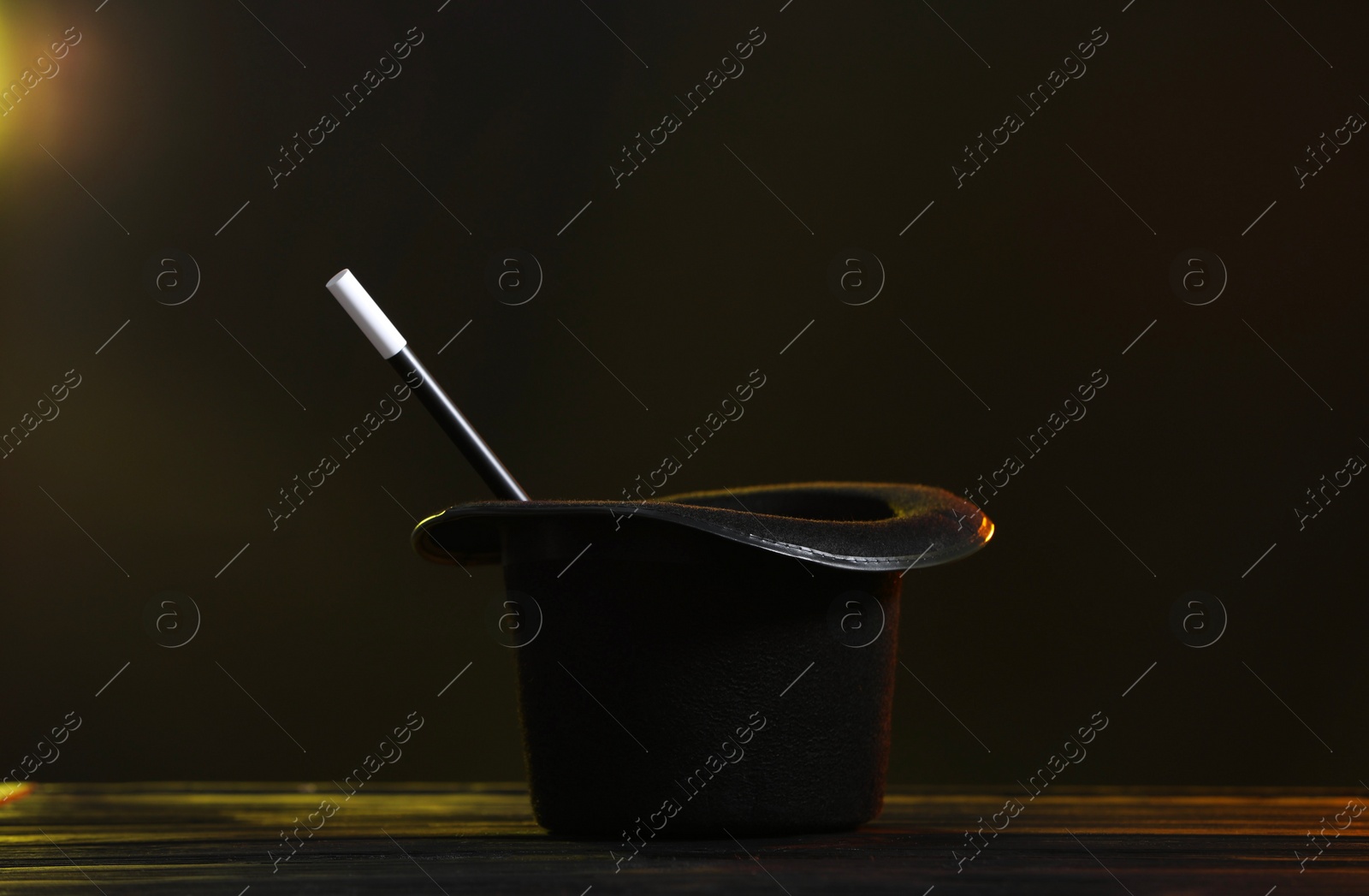 Photo of Magician's hat and wand on wooden table against dark background