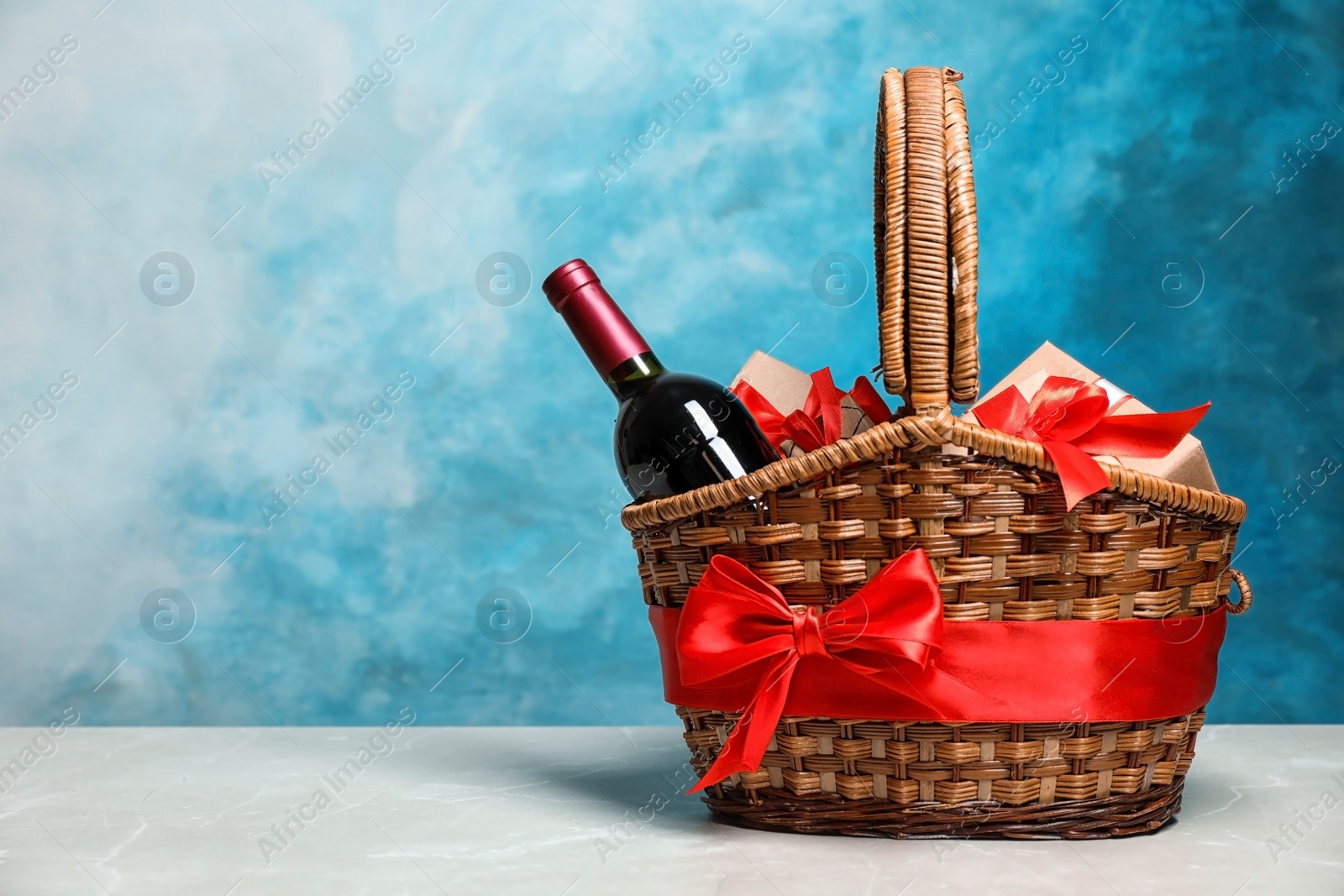 Photo of Gift basket with bottle of wine on color background. Space for text