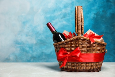 Gift basket with bottle of wine on color background. Space for text