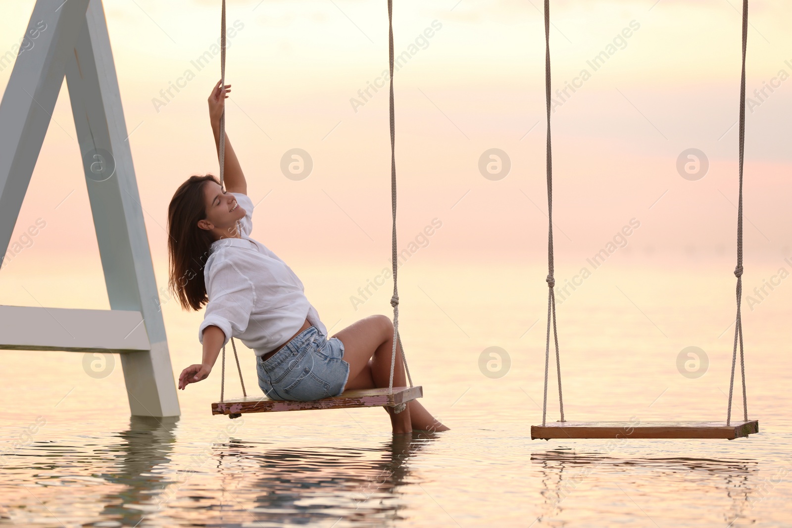 Photo of Young woman enjoying sunrise on swing over water