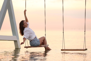 Photo of Young woman enjoying sunrise on swing over water