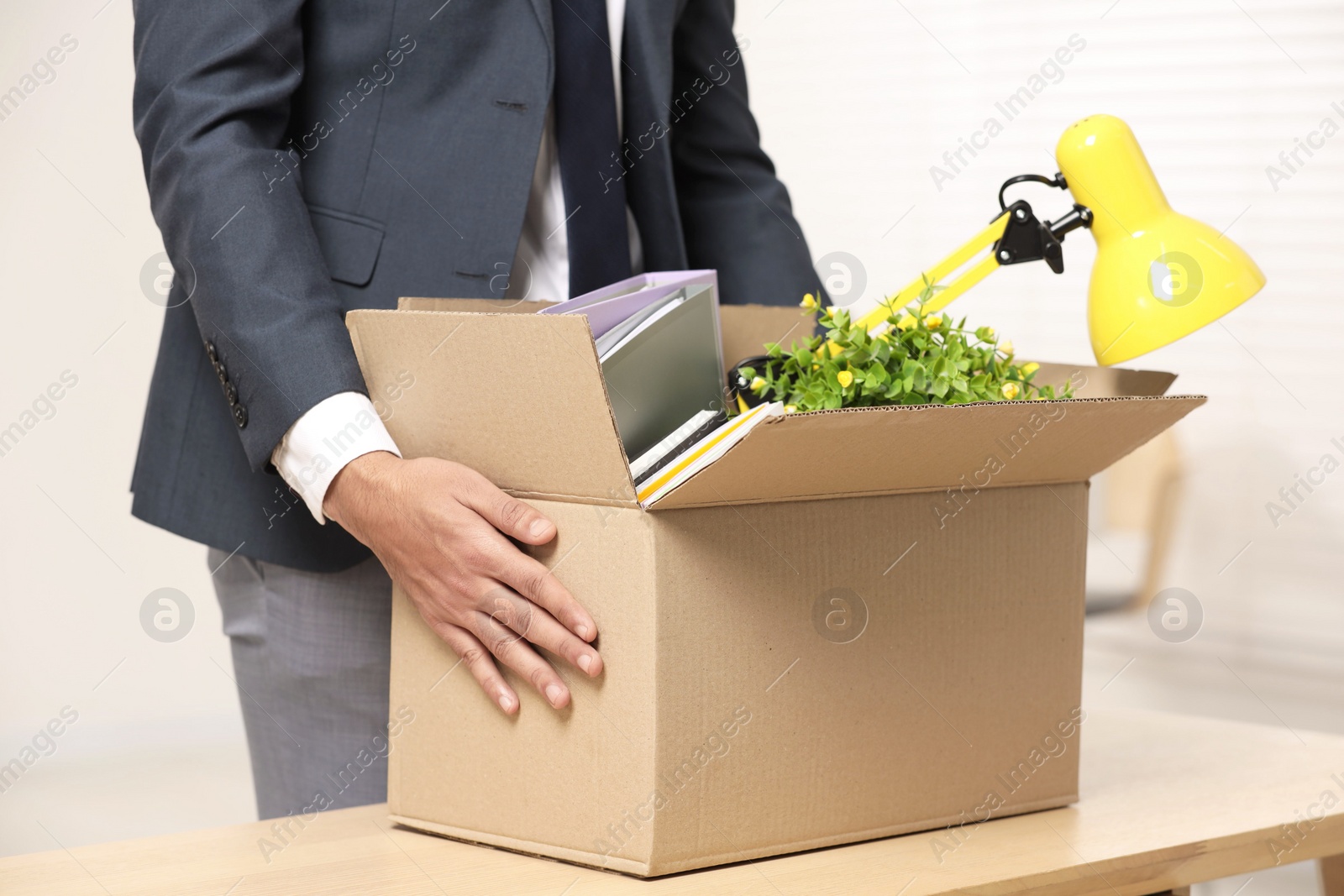 Photo of Unemployment problem. Man with box of personal belongings at table in office, closeup