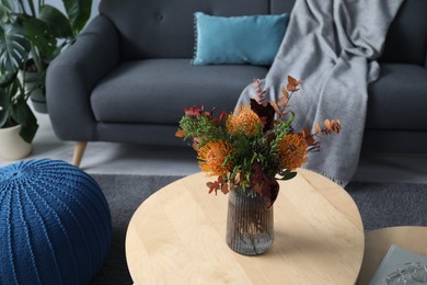 Vase with bouquet of beautiful leucospermum flowers on wooden nesting tables, sofa and ottoman indoors