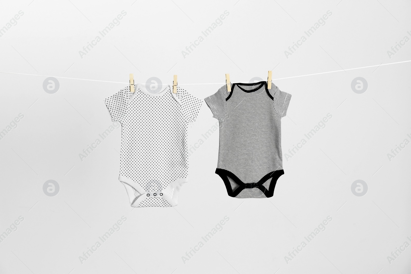 Photo of Different baby onesies hanging on clothes line against light grey background. Laundry day