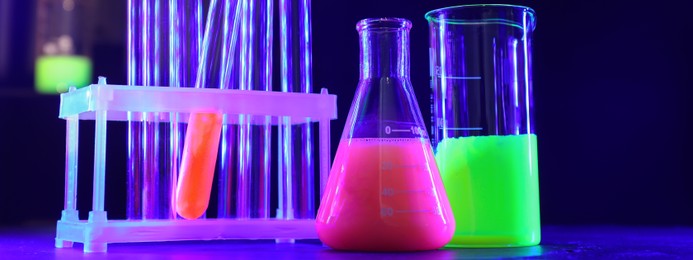 Image of Laboratory analysis. Different glassware with luminous liquids on table against dark background, banner design