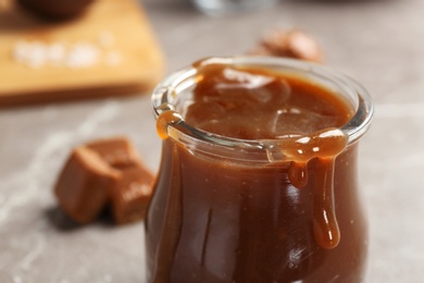 Photo of Jar with tasty caramel sauce on table, closeup