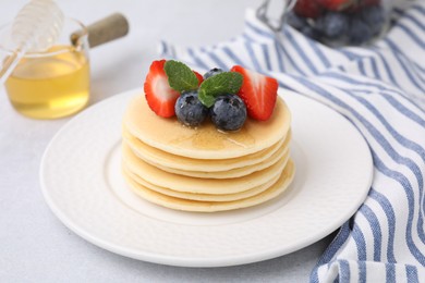 Delicious pancakes with strawberries, blueberries and honey on light grey table, closeup