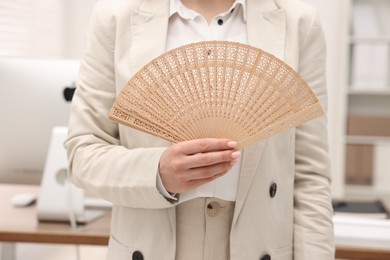 Businesswoman with hand fan in office, closeup