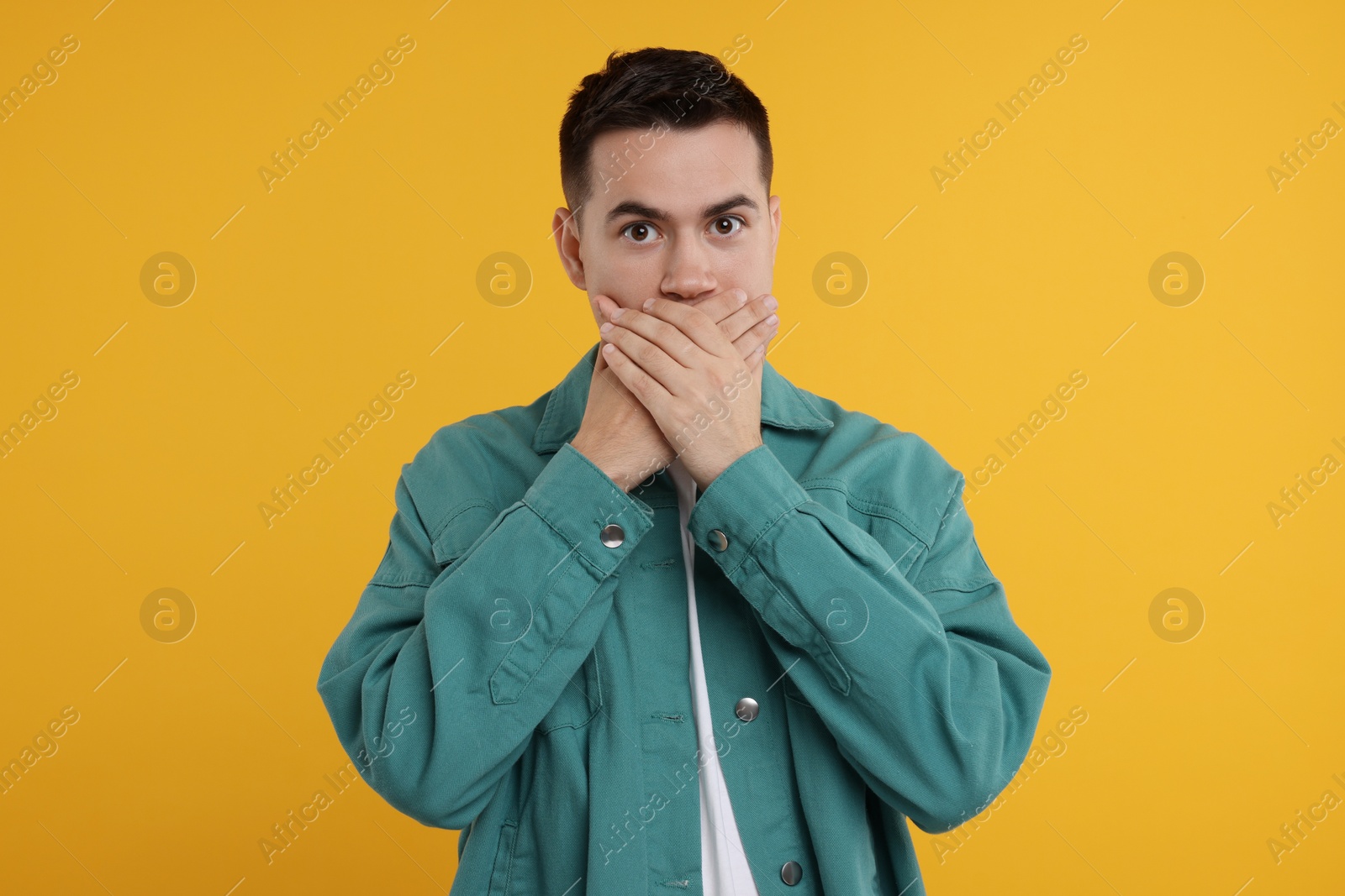 Photo of Embarrassed man covering mouth with hands on orange background