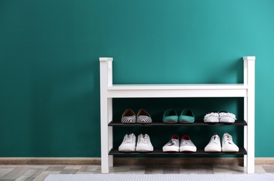 Photo of Shoe rack with different footwear near color wall, space for text. Stylish hallway interior