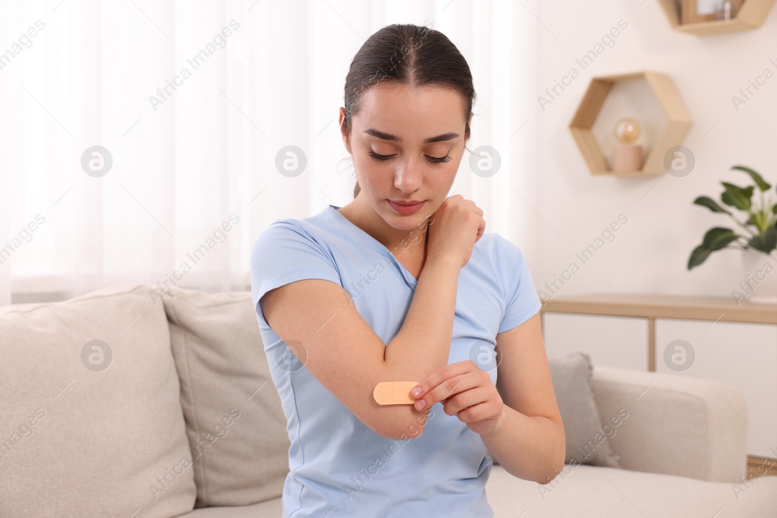 Photo of Woman putting sticking plaster onto elbow at home