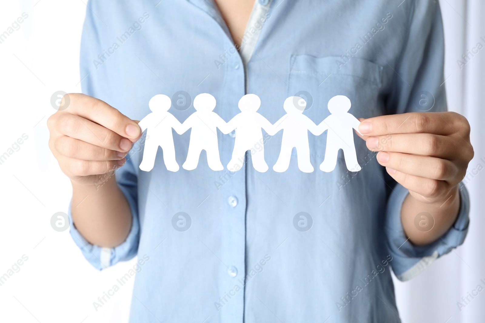 Photo of Woman holding paper people chain on light background, closeup. Unity concept