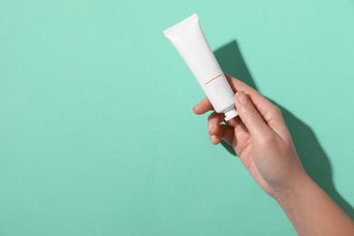 Photo of Woman with tube of hand cream on turquoise background, top view. Space for text