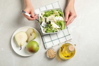 Photo of Woman eating fresh salad with pear at light table, top view