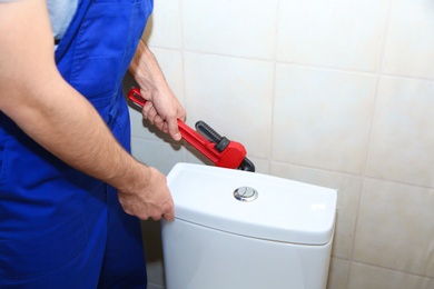 Photo of Male plumber repairing toilet tank in bathroom, closeup