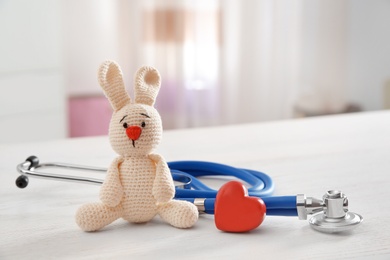 Photo of Toy bunny, stethoscope and heart on table indoors, space for text. Children's doctor