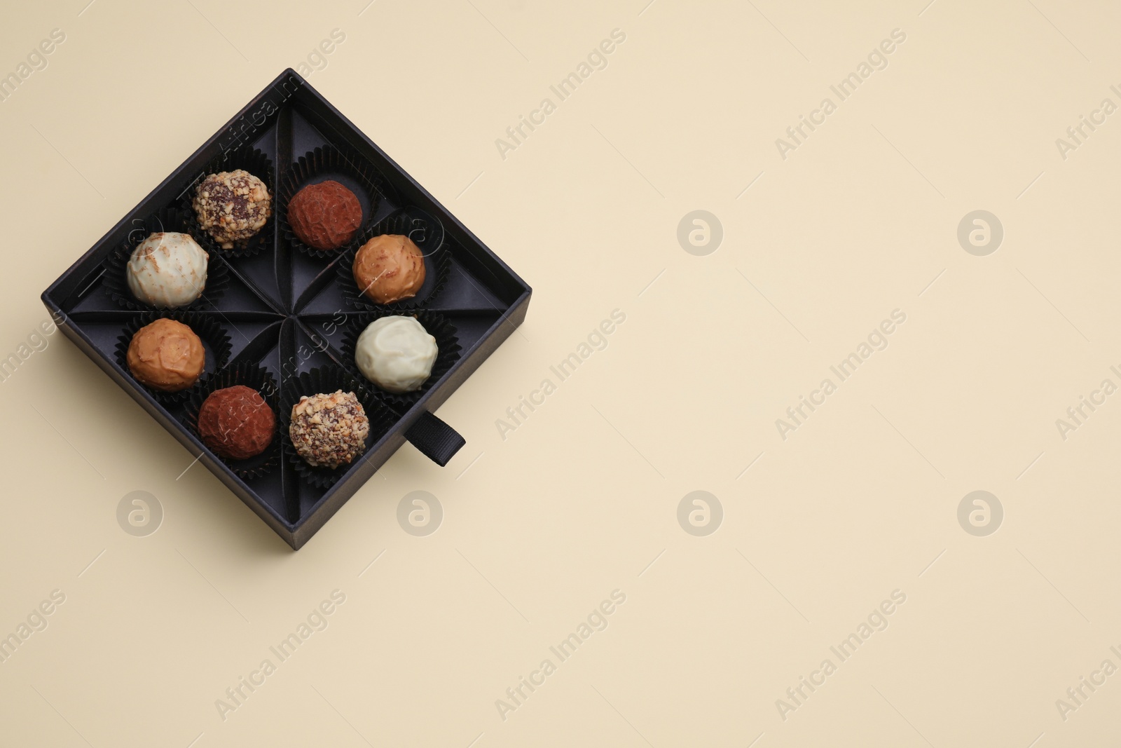 Photo of Box of tasty chocolate candies on beige background, top view. Space for text