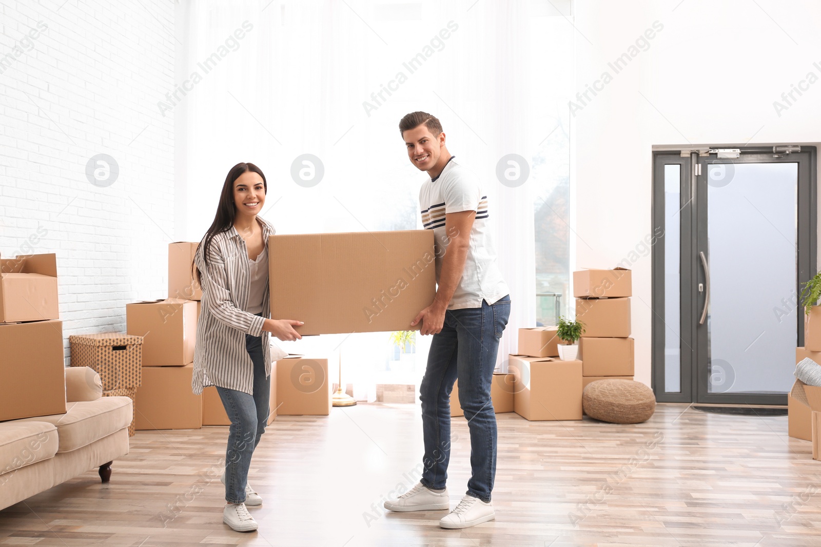 Photo of Happy couple in room with cardboard boxes on moving day