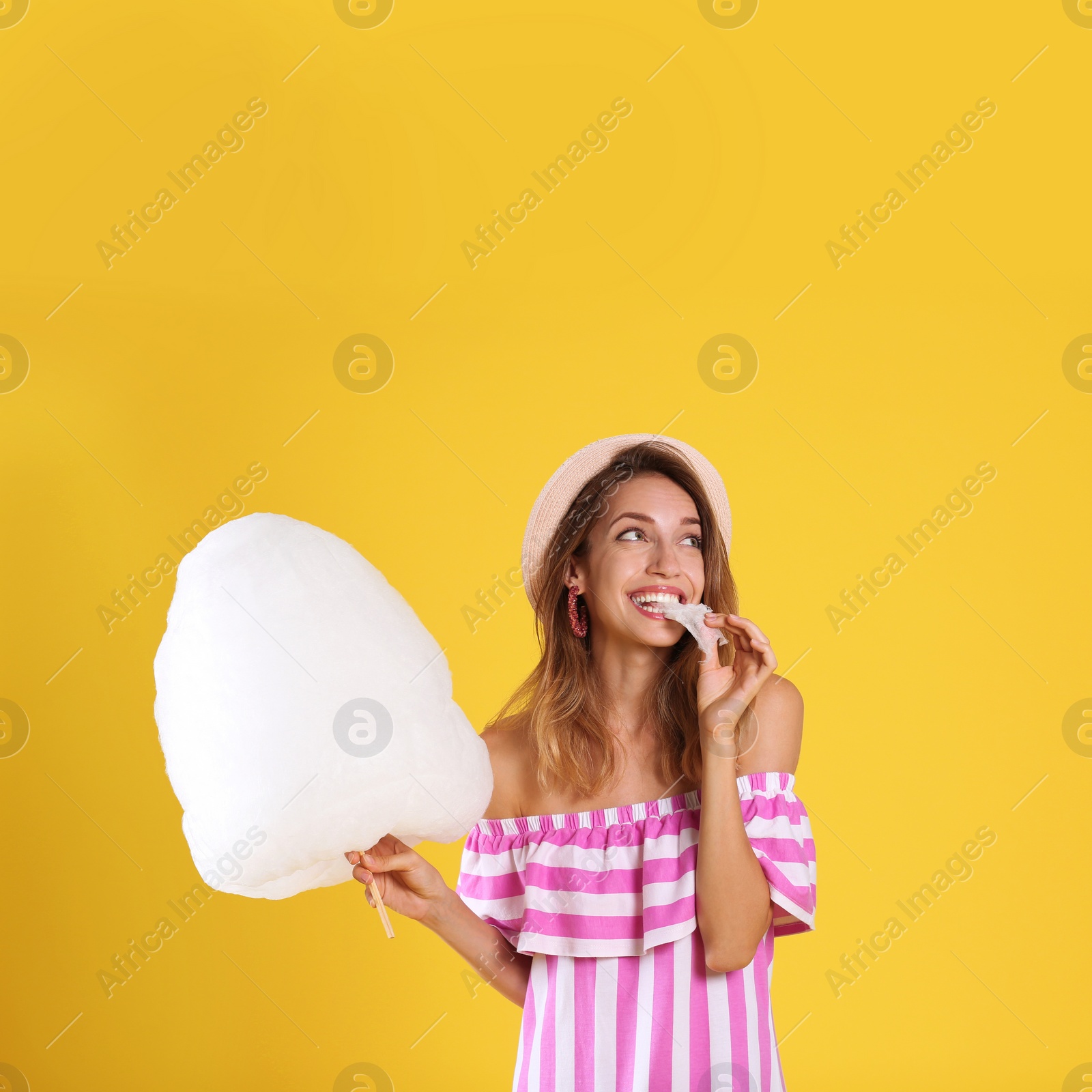 Photo of Happy young woman eating cotton candy on yellow background