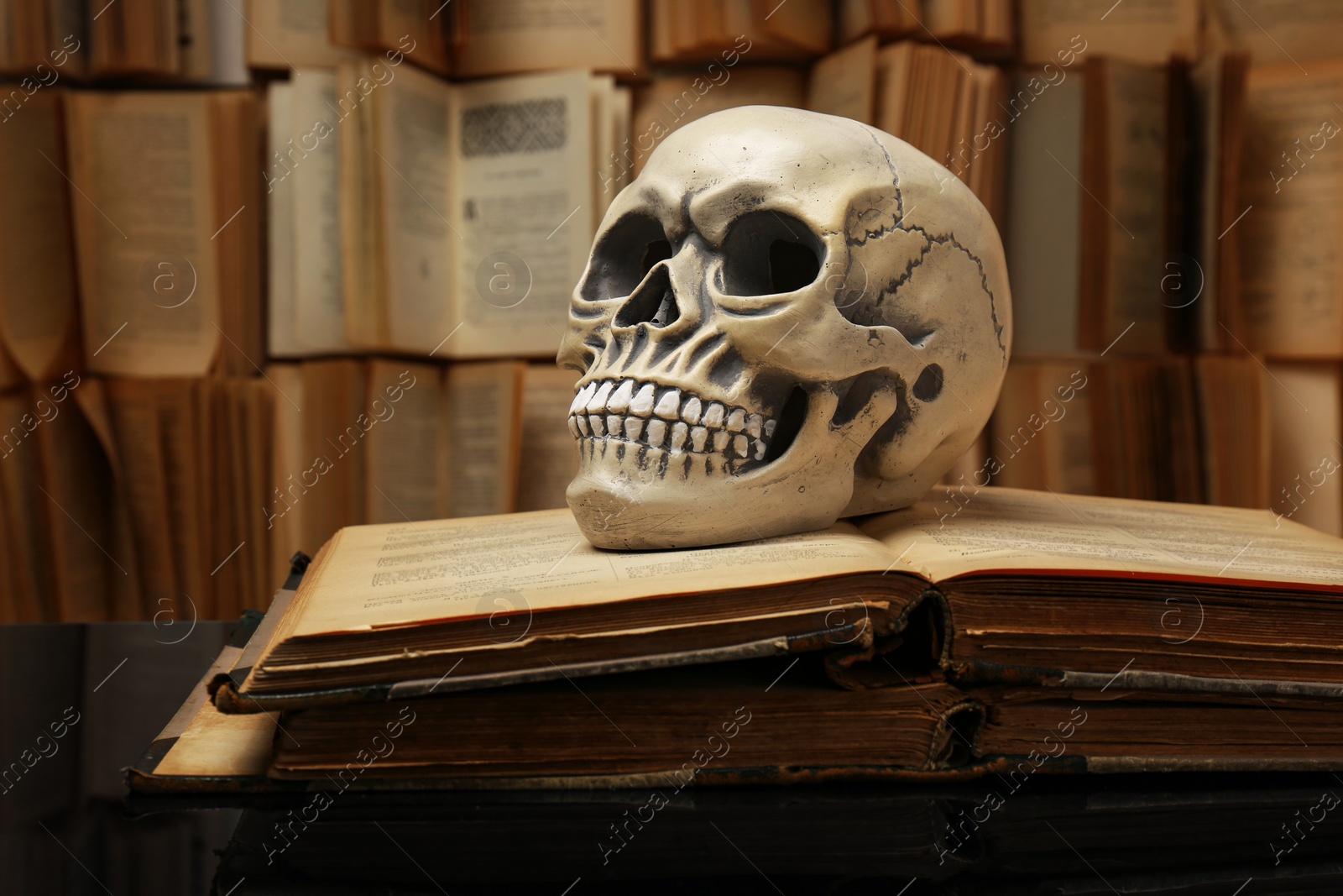 Photo of Human skull and old books on mirror table. Space for text