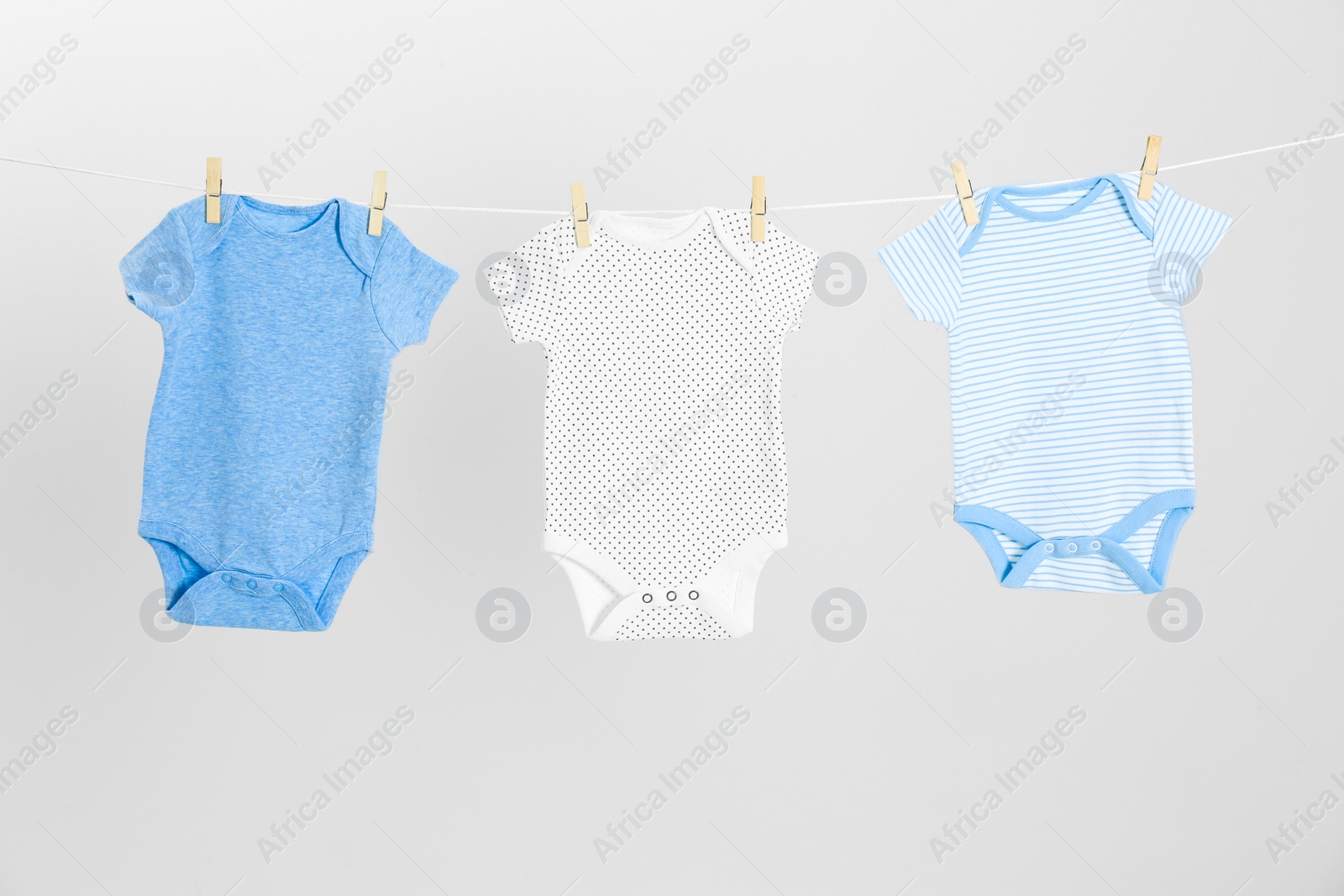 Photo of Different baby onesies hanging on clothes line against light grey background. Laundry day