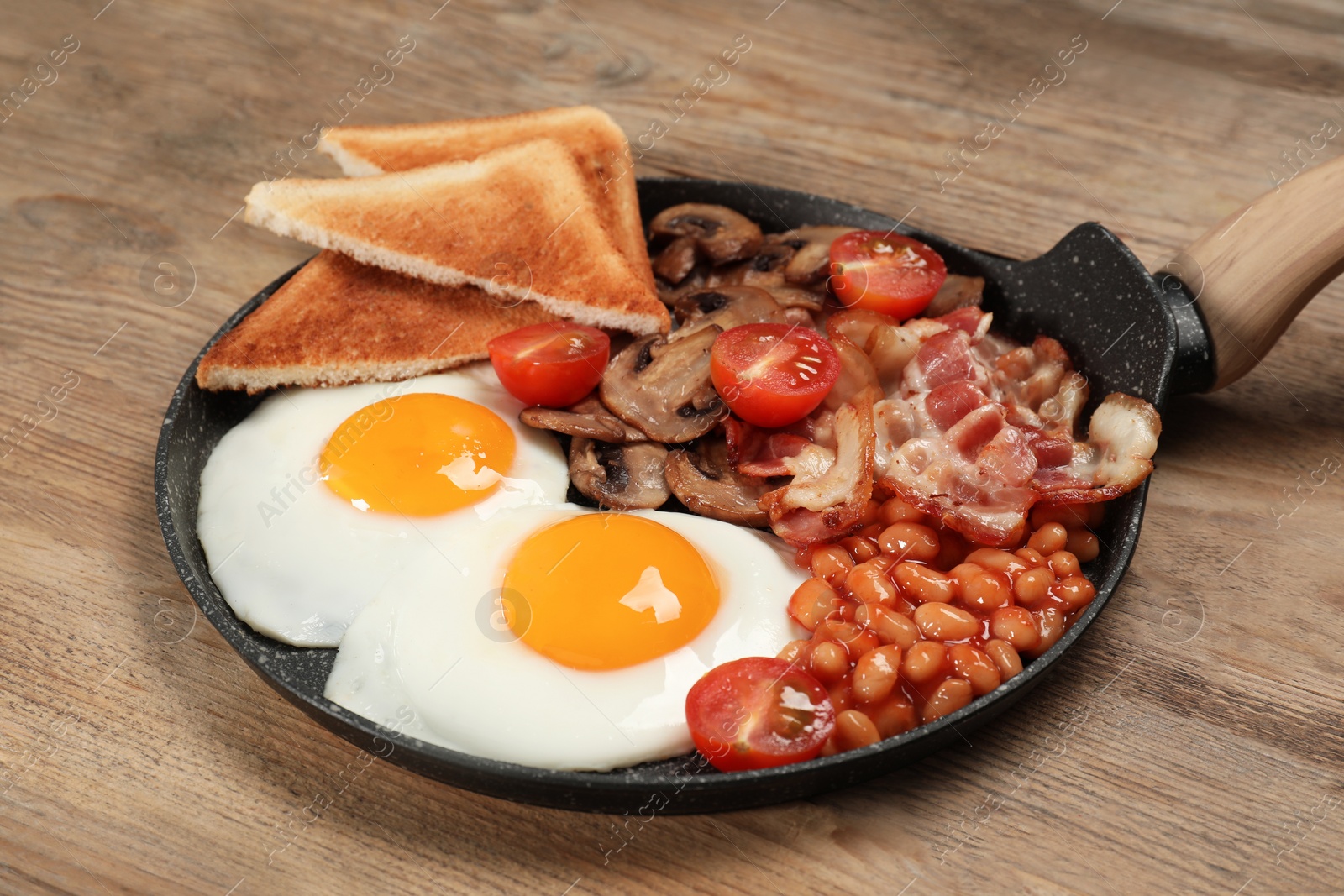 Photo of Serving pan with fried eggs, mushrooms, beans, bacon, tomatoes and toasted bread on wooden table, closeup. Traditional English breakfast