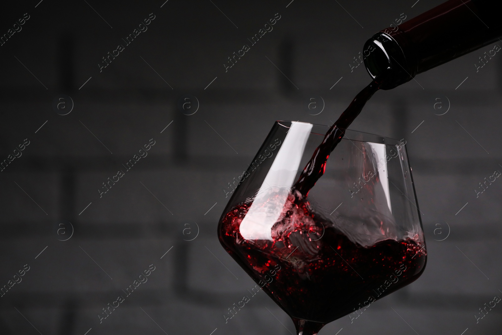 Photo of Pouring tasty red wine from bottle into glass against brick wall, closeup. Space for text