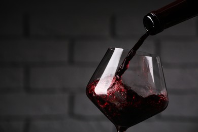 Photo of Pouring tasty red wine from bottle into glass against brick wall, closeup. Space for text