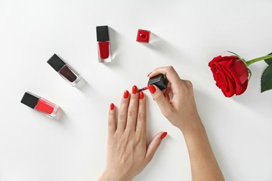 Woman applying bright nail polish on white background, top view