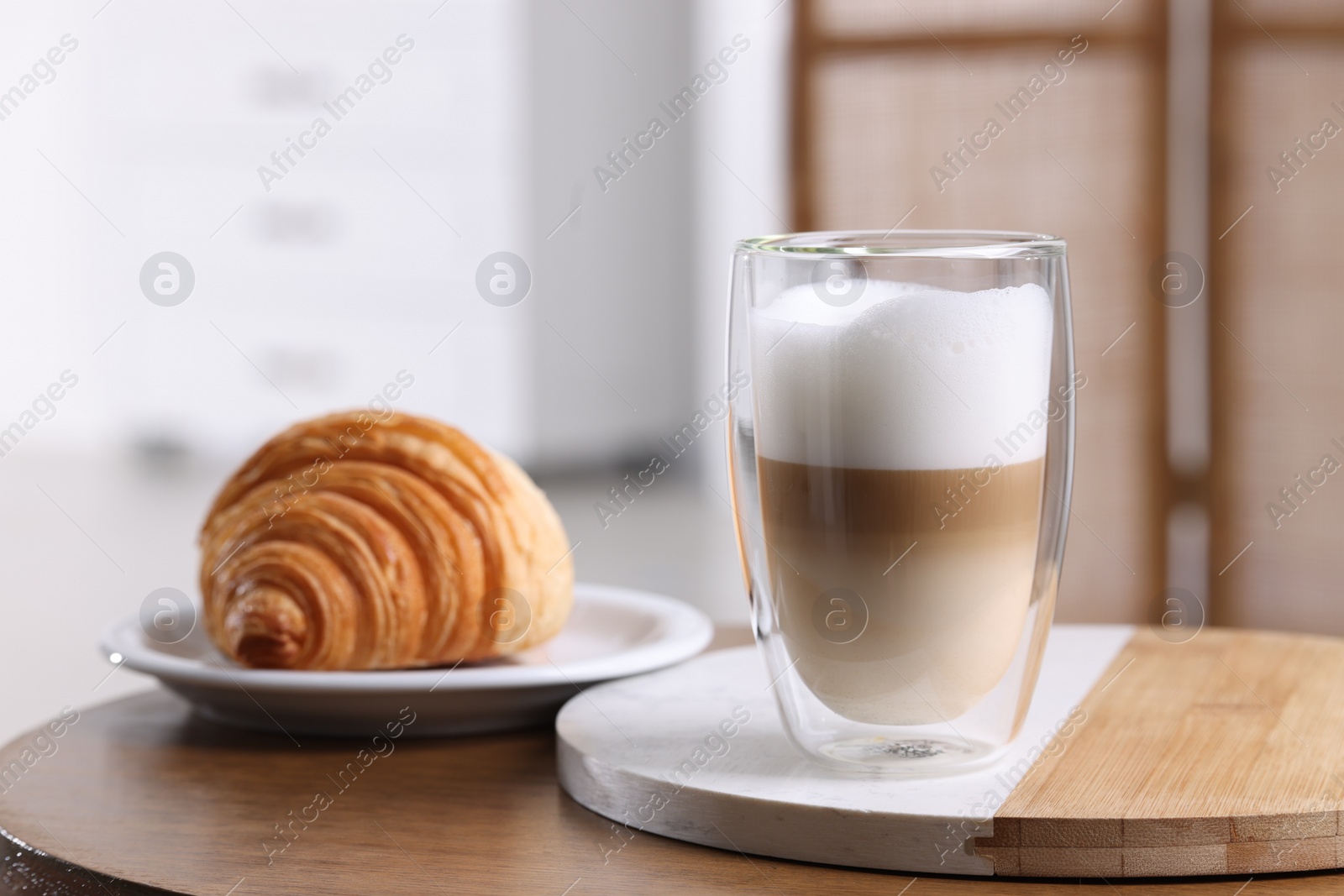 Photo of Aromatic latte macchiato in glass and croissant on wooden table against blurred background