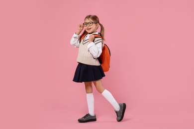 Happy schoolgirl in glasses with backpack on pink background