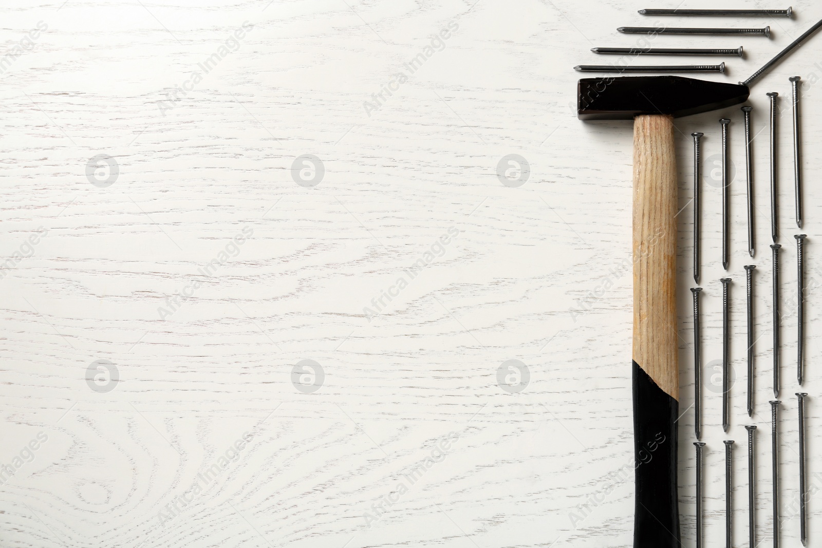 Photo of Hammer and metal nails on white wooden table, flat lay. Space for text