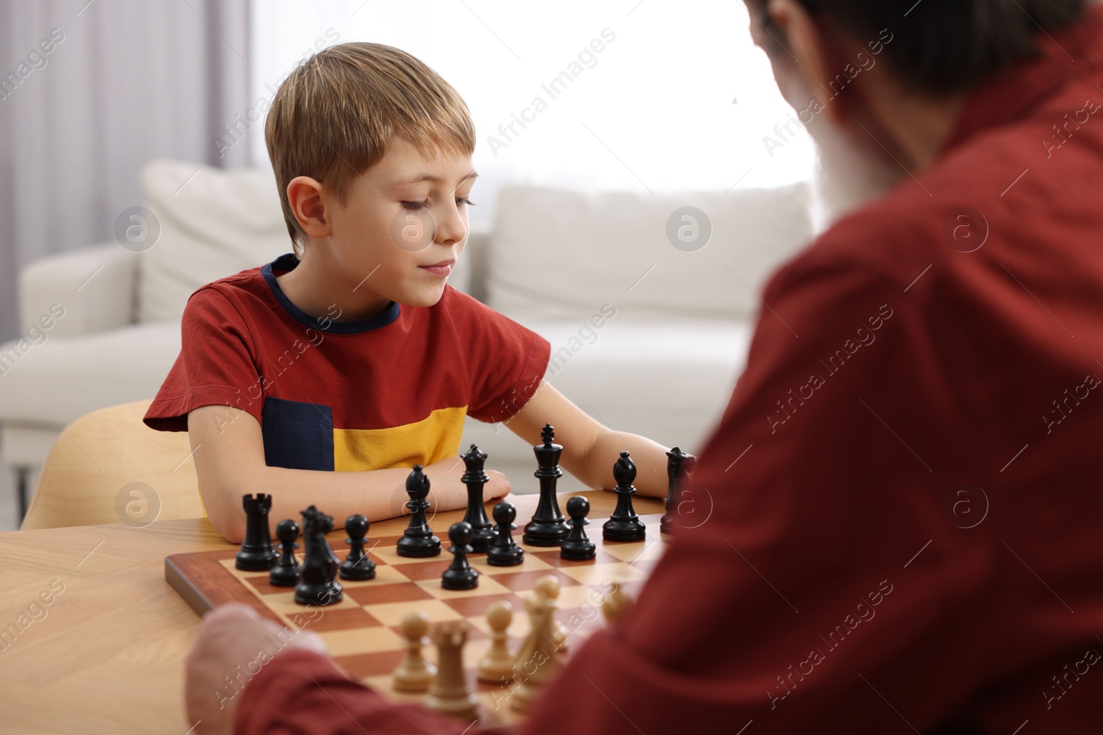 Photo of Little boy playing chess with his grandfather at table in room