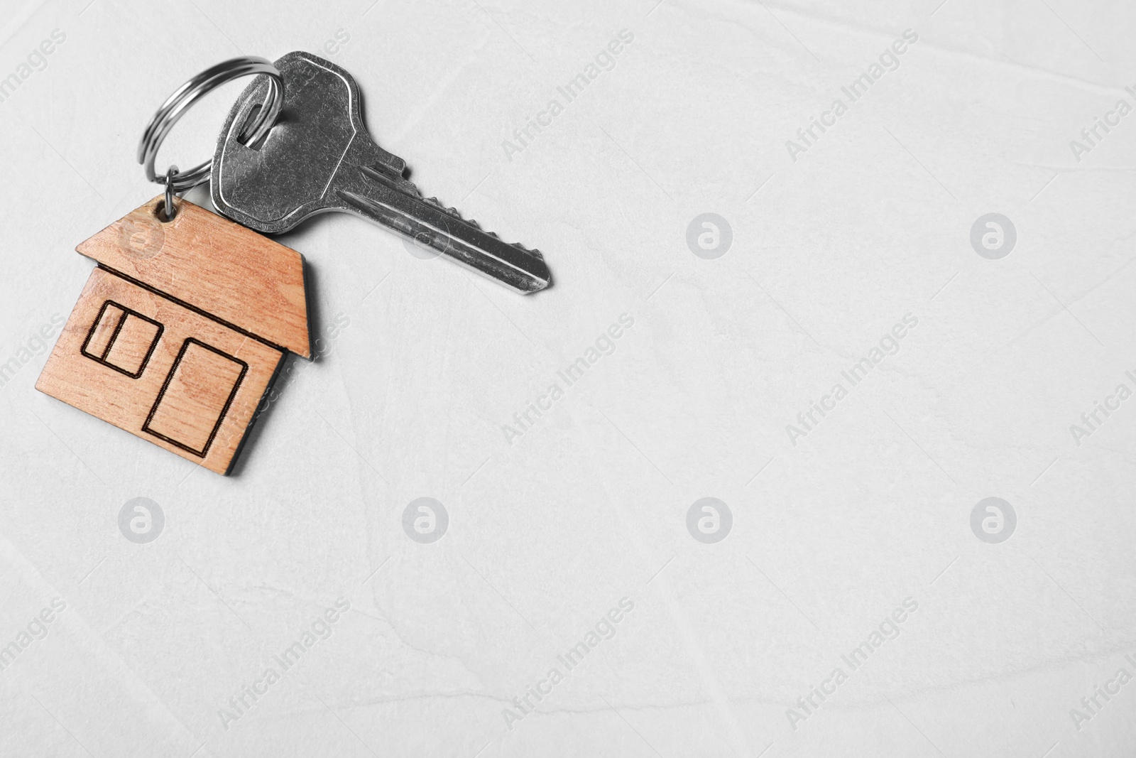 Photo of Key with trinket in shape of house on light grey stone background, top view and space for text. Real estate agent services