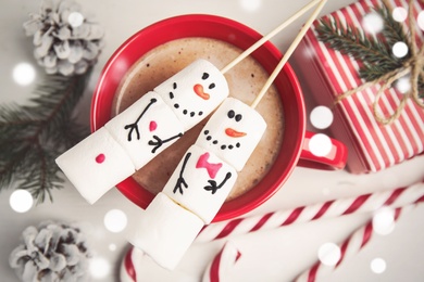 Photo of Flat lay composition with funny snowmen made of marshmallows in cup on white wooden table