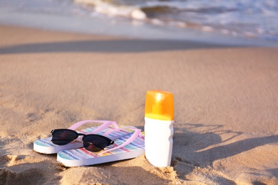 Photo of Flip flops and beach accessories on sand near sea. Space for text