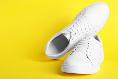 Photo of Pair of stylish white sneakers on yellow background. Space for text