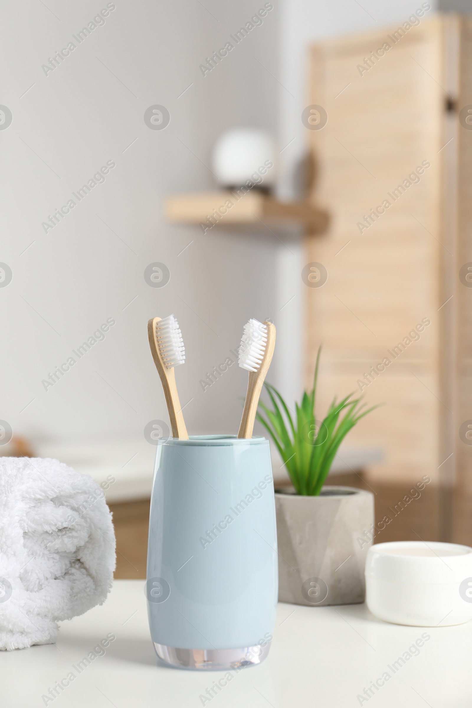 Photo of Bamboo toothbrushes, towel, potted plant and cosmetic product on white countertop in bathroom