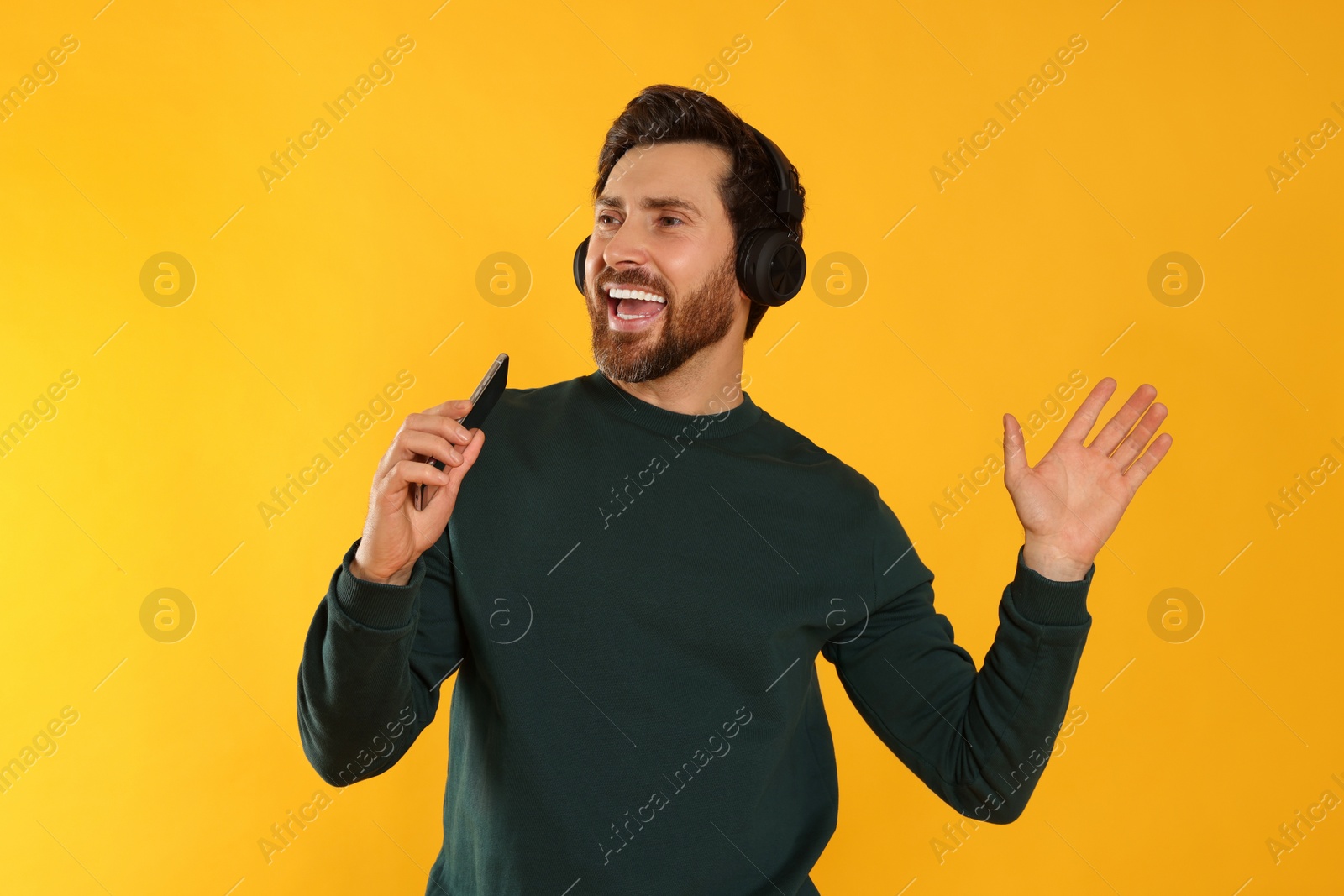 Photo of Happy man listening music with headphones on yellow background