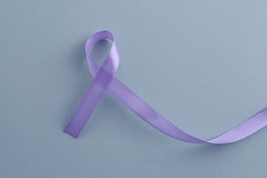 Violet awareness ribbon on light blue background, top view