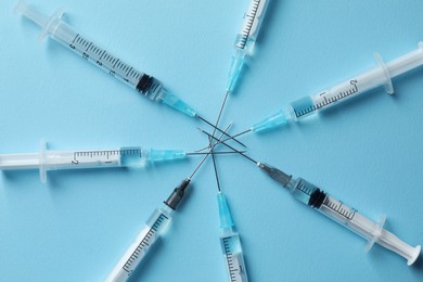 Photo of Disposable syringes with needles and medicine on light blue background, flat lay