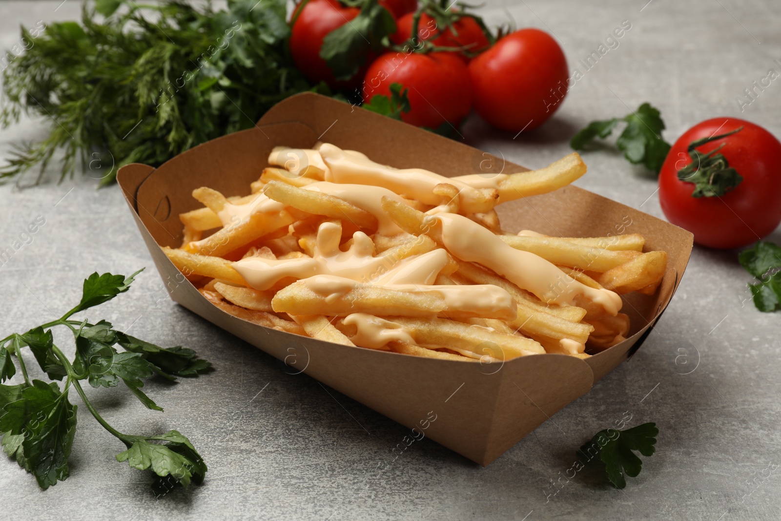 Photo of Tasty potato fries, cheese sauce in paper container and products on grey table, closeup