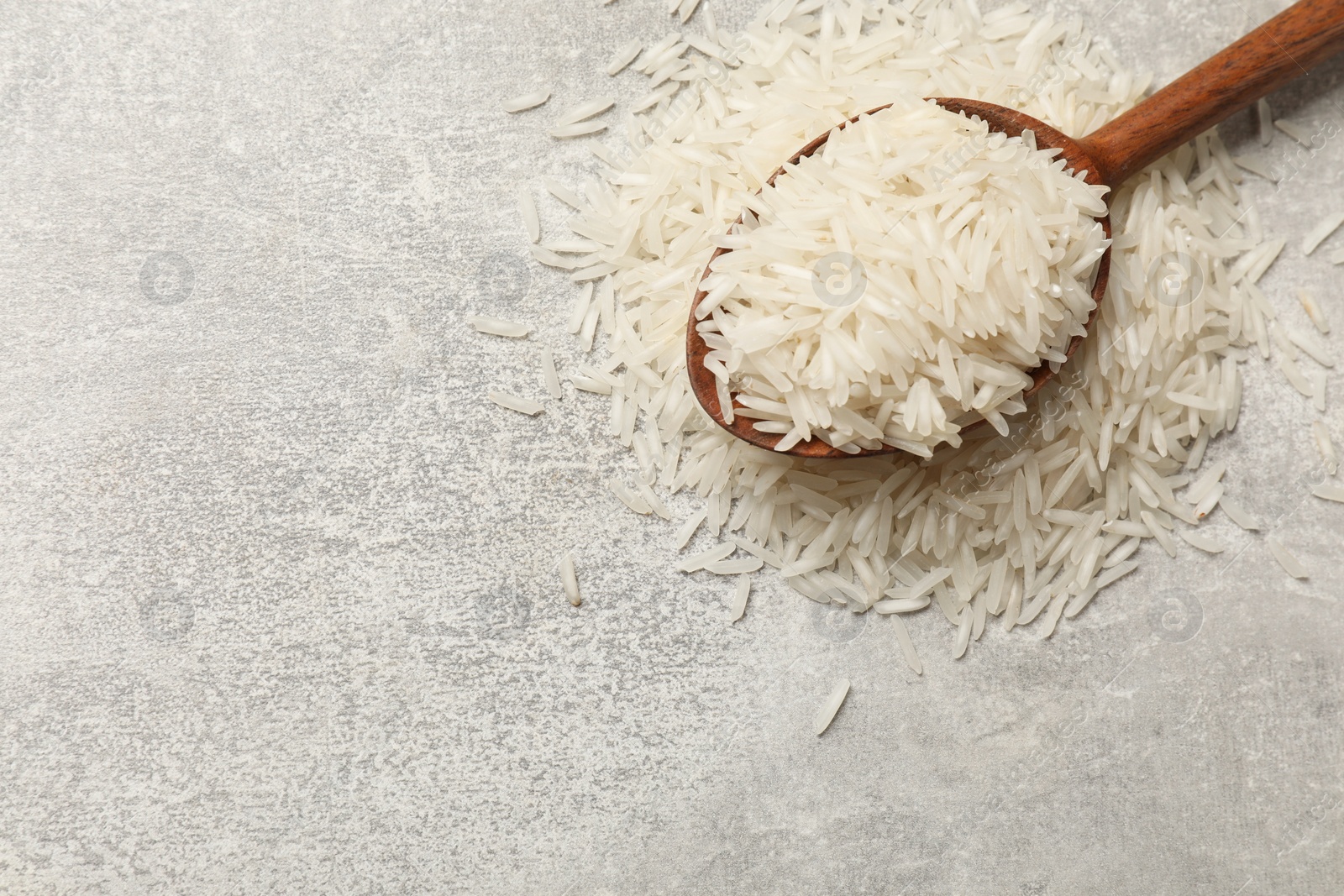 Photo of Raw basmati rice and wooden spoon on grey table, top view. Space for text