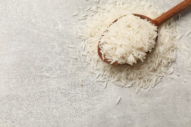 Photo of Raw basmati rice and wooden spoon on grey table, top view. Space for text