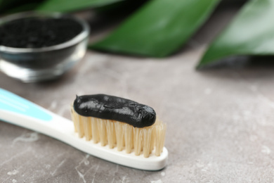 Photo of Toothbrush with natural bristles and charcoal paste on grey marble table, closeup